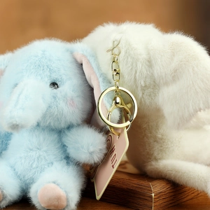 Close-up of blue and white plush elephant keychains with gold metal rings on wooden base
