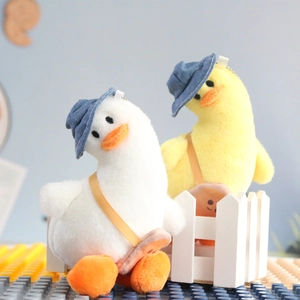 Detail view of plush duck keychains in white and yellow wearing denim hats and smiley bags