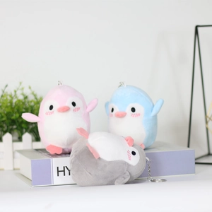 Plush penguin keychains in pink, blue, and grey stacked on a purple book