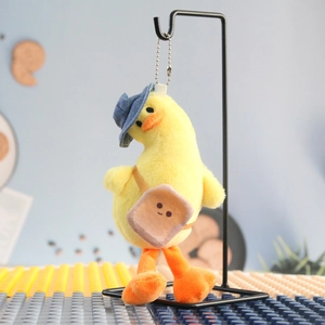 Detail of yellow duck plush keychain with blue sun hat and toast bag on black metal stand