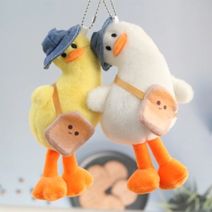 Detail of plush duck keychains in white and yellow wearing hats and toast crossbody bags
