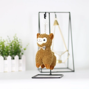 Detailed view of plush alpaca keychain in brown with plaid bow on a black metal stand