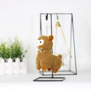 Close-up of brown plush alpaca keychain with a plaid bow hanging on a metal stand