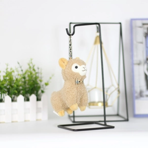 Close-up of brown alpaca plush keychain with checkered bow tie on a metal display stand
