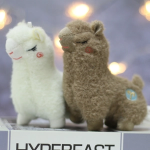 Detail of white and brown plush alpaca keychains with cute embroidery on a prop book