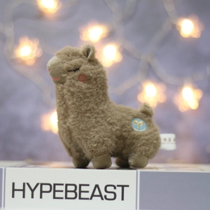 Detail of a brown alpaca plush with curly fur and a gold Aries zodiac embroidery