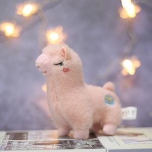 Detailed view of pink alpaca plush keychain with embroidery and soft bokeh background