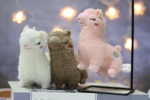 Close-up of cute alpaca plush keychains in white, brown, and pink with fluffy texture