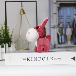 Pink plush pony keychain with metal chain resting on a book in a cozy home setting