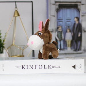 Detail shot of a brown plush donkey keychain accessory on a white book with decor