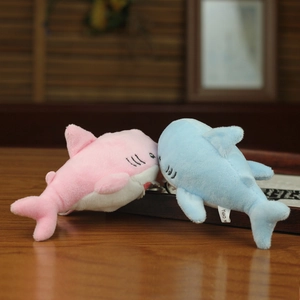 Detail of pink and blue plush shark charms with metal hooks on a wooden surface