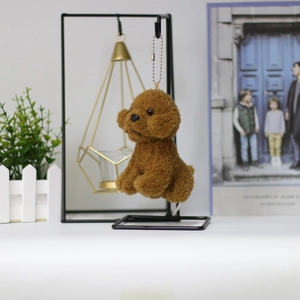 Close-up of curly brown plush teddy dog keychain with silver chain on a metal stand