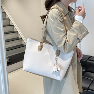 Ivory leather tote bag with khaki straps and bow charm shown in a modern interior setting