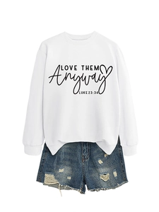 Close-up of white crewneck sweatshirt with Love Them Anyway text and ripped denim shorts