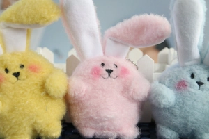 Close-up of plush rabbit charms in pink, yellow, and blue with bead chains for hanging