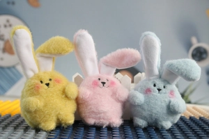 Close-up of plush rabbit pendants in pastel yellow, pink, and blue with bead chains