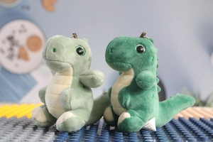 Close-up of cute green plush dinosaur keychains with metal chains on a textured surface