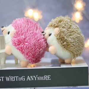 Cute pink and brown plush hedgehog keychains shown on miniature chairs in warm lighting