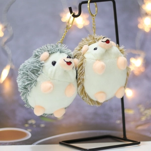 Cute plush hedgehog keychains in dark grey and light brown on a metal display stand
