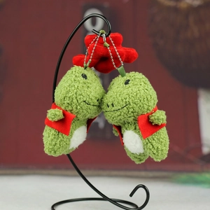 Détail de mignons pendentifs dinosaures en peluche verte avec gilets rouges et chaînettes