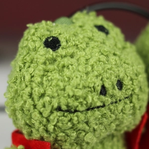 Gros plan macro du pendentif grenouille en peluche verte montrant la texture douce