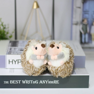 Cute brown plush hedgehog keychain pair sitting on decorative books for backpack charm