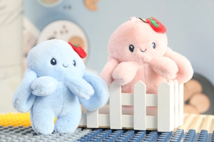 Close-up of pink and blue plush rabbit keychains with strawberry hats on a white fence
