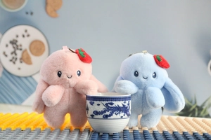Detail of pink and blue plush bunny keychains with strawberry hats on a table