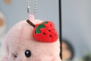 Macro shot of pink plush keychain with strawberry embroidery and silver bead chain