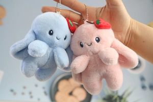 Close-up of plush rabbit pendants in pink and blue with strawberry embroidery and ball chain