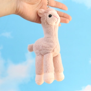Pink alpaca plush keychain with silver chain held against a blue sky background