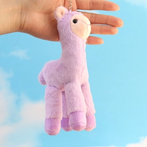 Detail of a purple plush alpaca keychain with metal ring held against a blue sky background