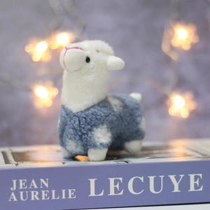 Macro detail of a plush white alpaca keychain with blue polka dot jacket on a gift box