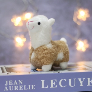 Close-up of a soft white and brown plush alpaca doll on a decorative book base