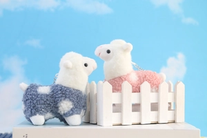 Close-up of pink and blue alpaca plush keychains with metallic hooks on a decorative stand