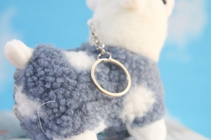 Detail of cute alpaca plush keychain wearing a blue polka dot knitted sweater with silver ring