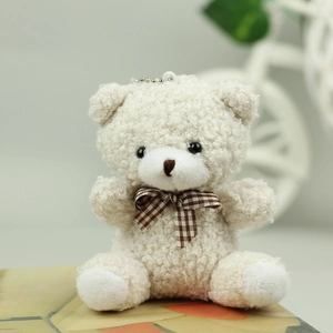 Detail of cream plush teddy bear with curly fur and brown checkered bowtie keychain