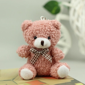 Close-up of a pink plush teddy bear keychain with a brown plaid bow and metallic chain