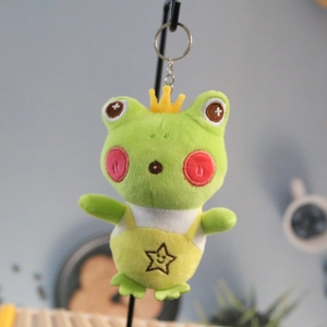 Close-up of green plush frog keychain with yellow crown and star overalls detail