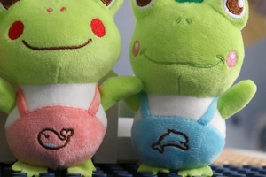 Close-up of cute green frog plush toys with pink whale and blue dolphin embroidery details