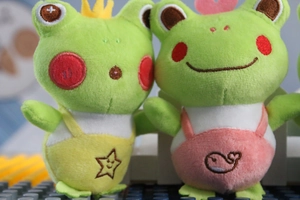 Close-up of cute green plush frogs wearing yellow and pink overalls with fine embroidery