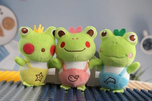 Detailed view of three cute plush frogs with colorful overalls and embroidery icons