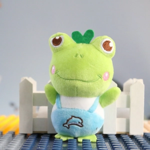 Macro detail of a plush green frog keychain with blue overalls and heart leaf