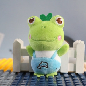 Detail of green plush frog keychain with blue dolphin overalls and heart headwear