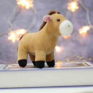 Close-up of a mini brown plush pony keychain standing on a book with bokeh lights