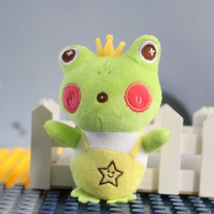 Close-up of green plush frog keychain wearing a yellow crown and star overalls