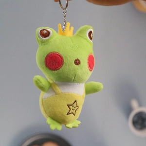 Detail of cute long-legged frog plush keychain with yellow crown and star overalls