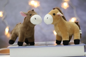 Close-up of cute plush horse keychains in brown and khaki with metal hooks on a book
