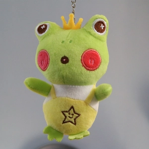 Detail of frog plush keychain with yellow crown and star patterned overalls on blue background
