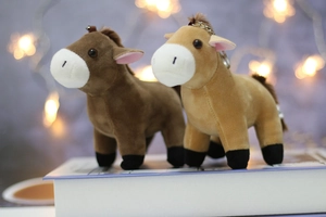 Close-up of plush pony keychains in brown and khaki with metal rings on a white book